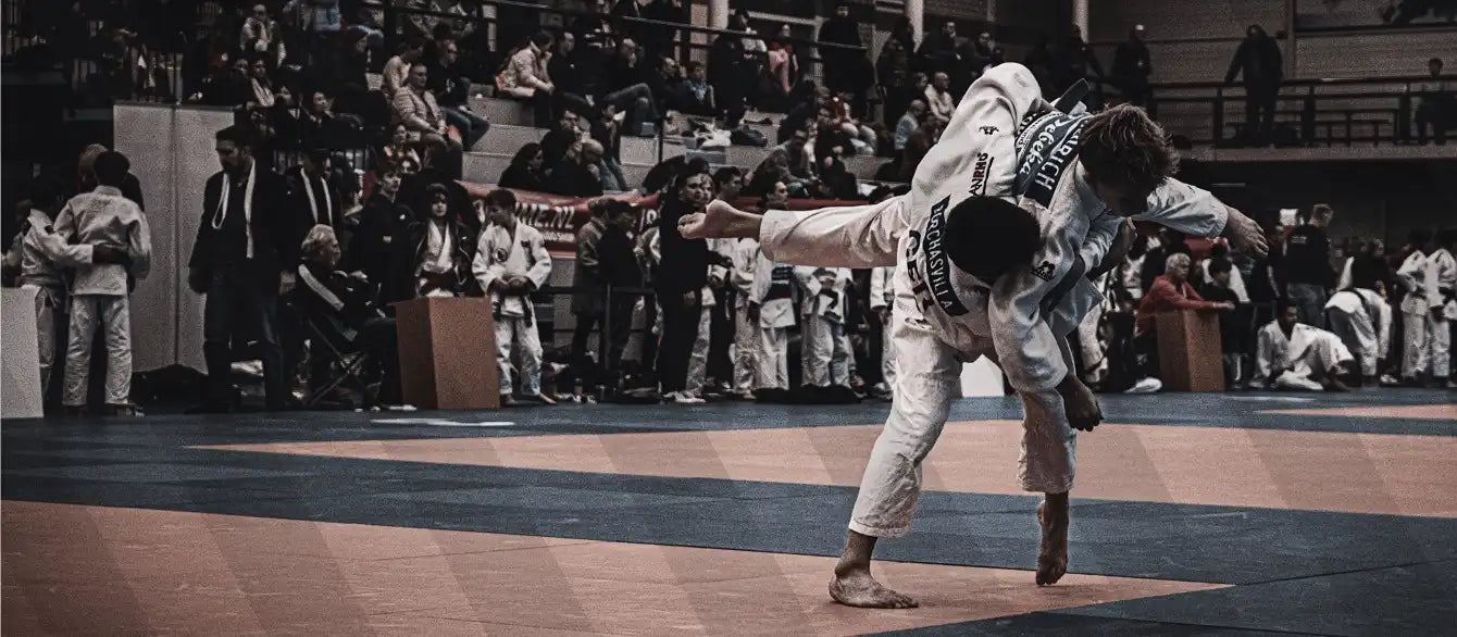 Judokas in weißem Anzug, die einen Wurf vor Publikum während eines Wettkampfs ausführen